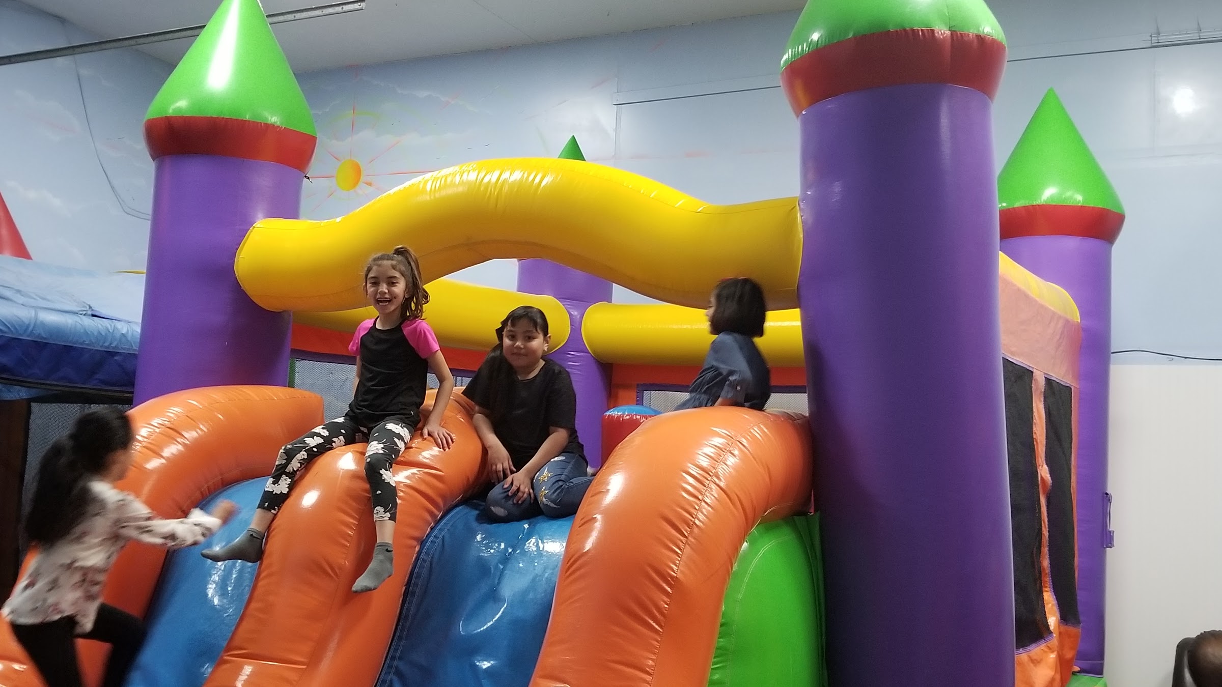 Two girls laughing as they slide down a colorful inflatable bounce castle at Inflatable Fun Gym