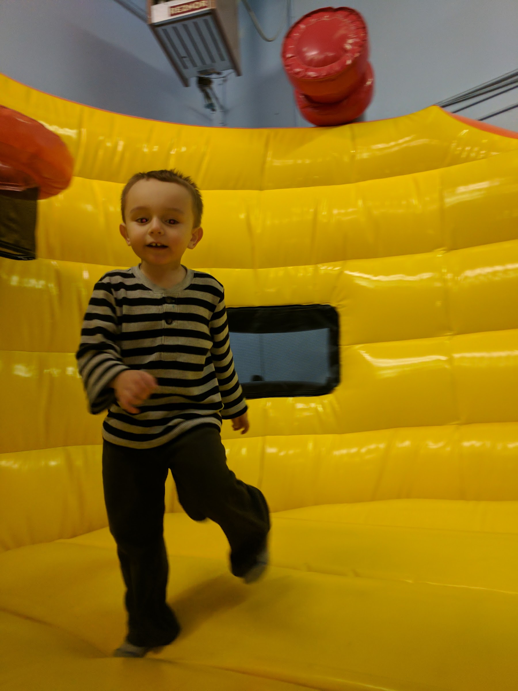A young boy running and smiling inside a yellow bounce house at Inflatable Fun Gym